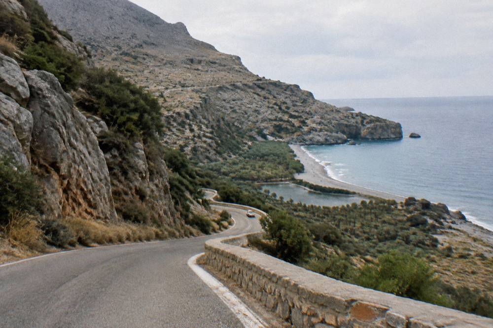 A winding mountain road descending through rocky hills toward the sea