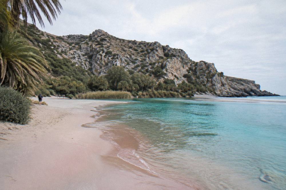 A shallow lagoon shoreline with pale pink sand and calm turquoise water