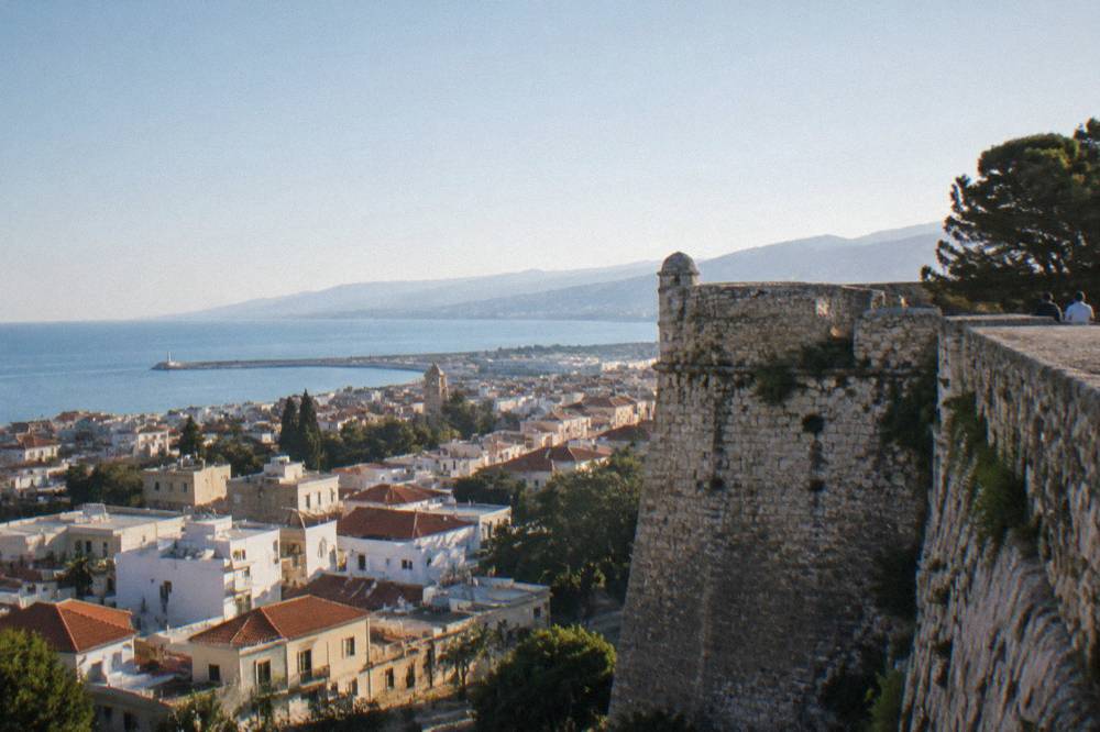 A stone fortress wall standing above dense town rooftops under a clear sky