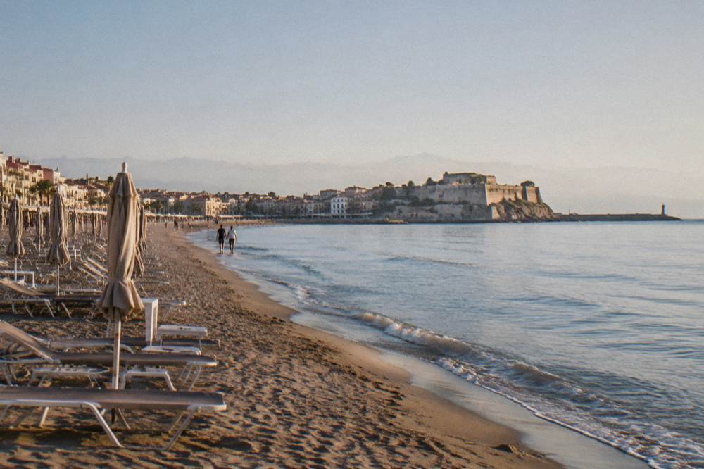 A wide sandy beach along a town seafront with sunbeds and calm water