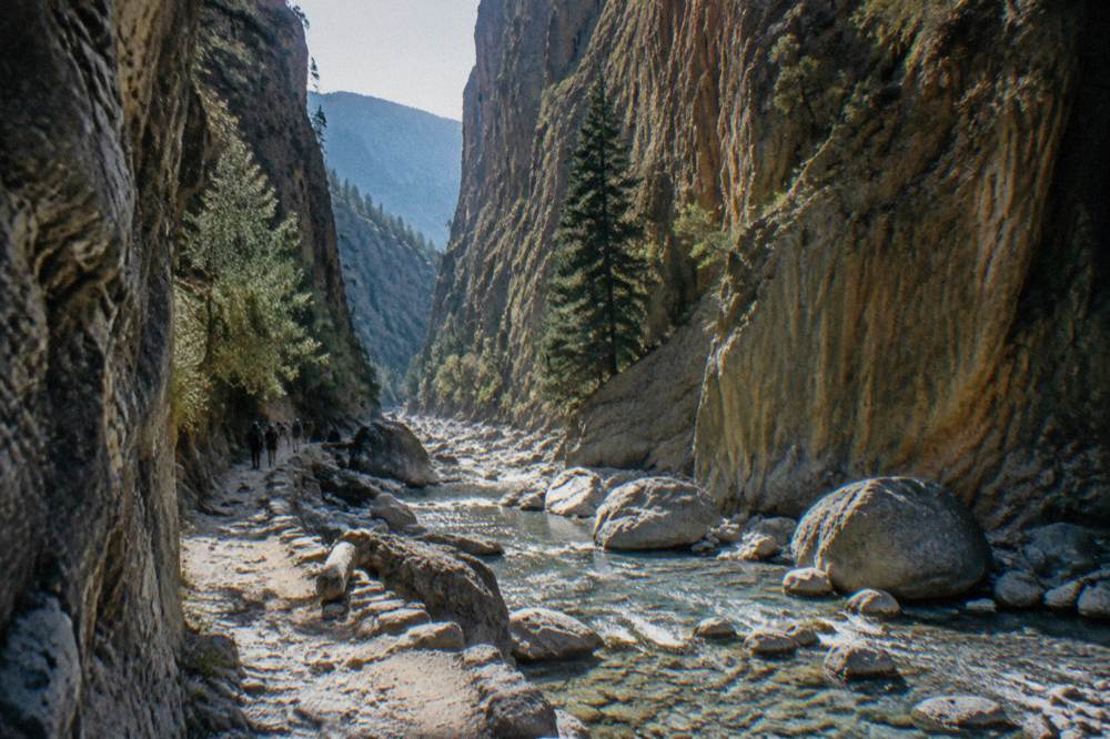 A narrow gorge passage with sheer rock walls rising above a stony stream bed