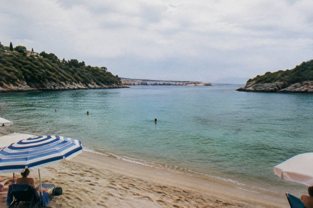 A calm circular bay with clear shallow water, green headlands and a handful of umbrellas