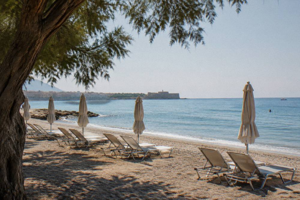 An empty sunbed row on a beach in early morning light with calm water beyond