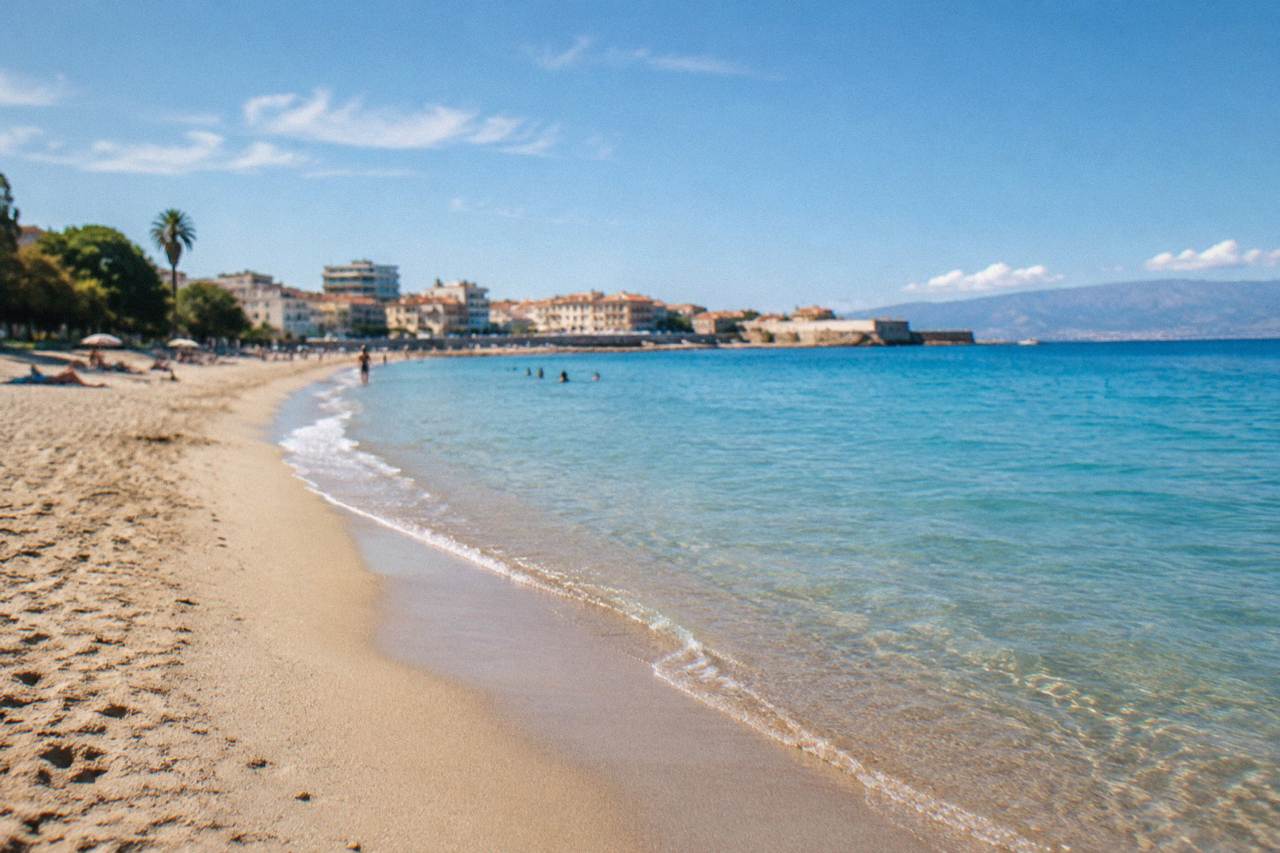 A sandy beach curving away from a small city with calm turquoise water close to shore