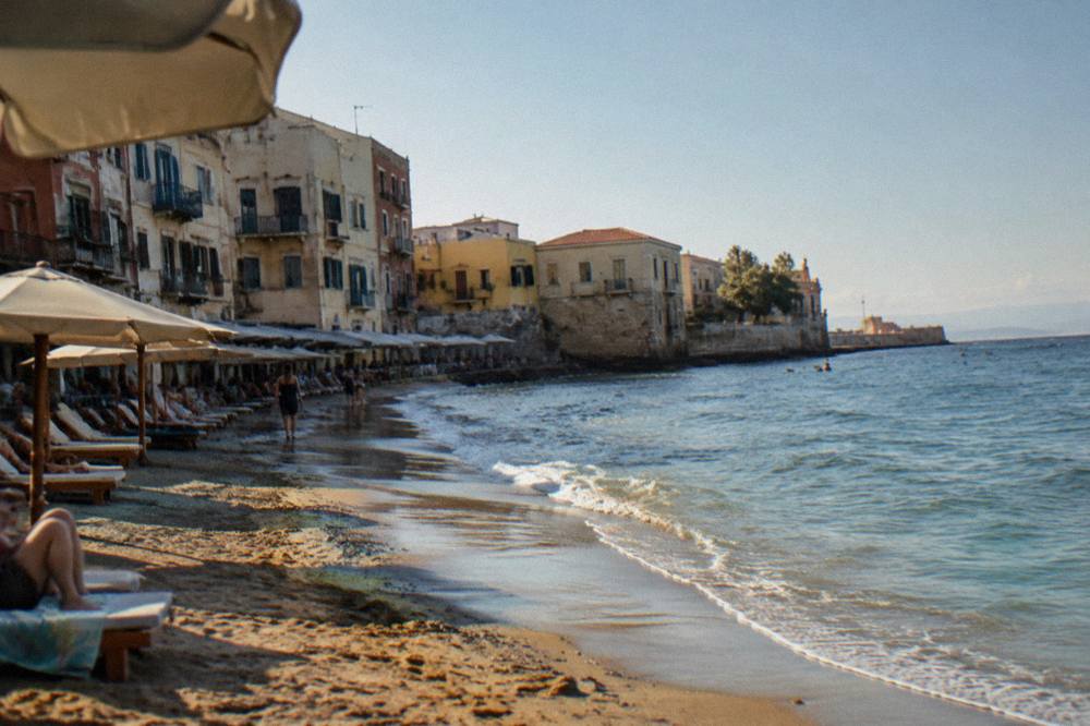 A narrow sandy beach directly below old townhouses with sun umbrellas along the water line
