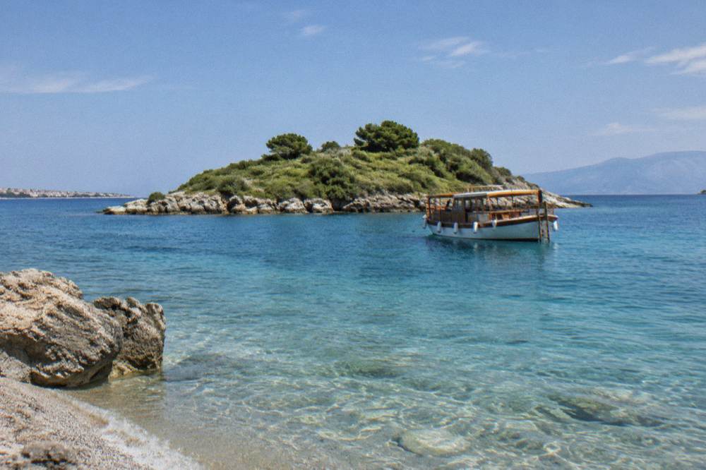 A small wooden excursion boat anchored off a tiny green island with clear shallow water