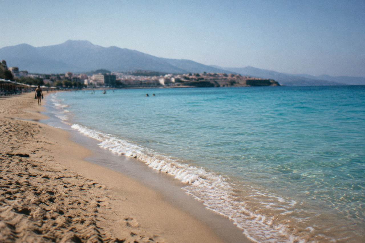 A wide sandy beach with turquoise shallow water and hills in the background on a clear day