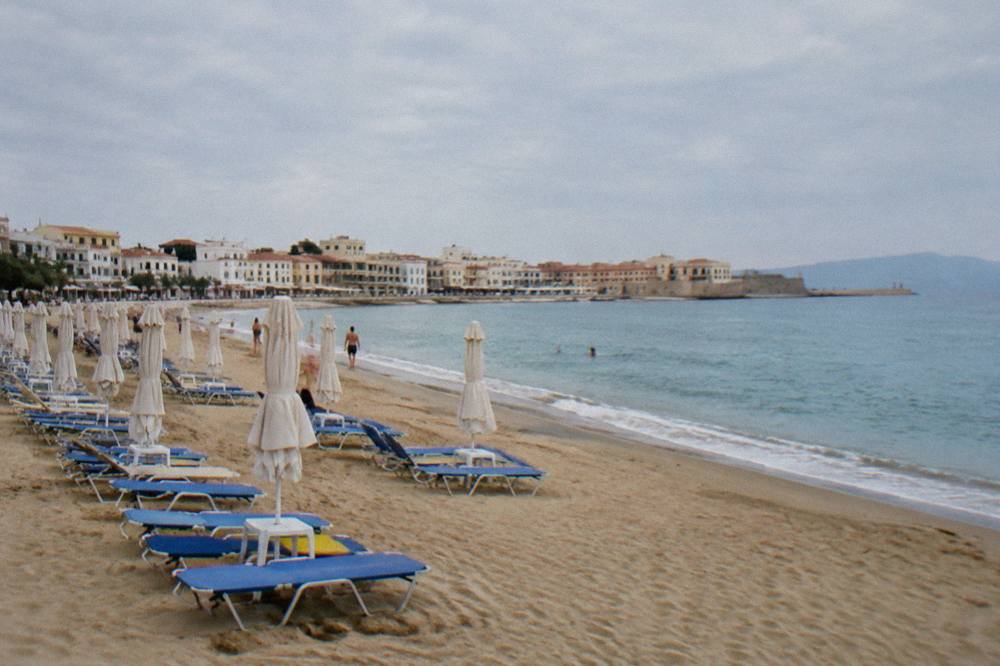 A long sandy beach with sunbeds in rows and calm blue water along a developed coastline