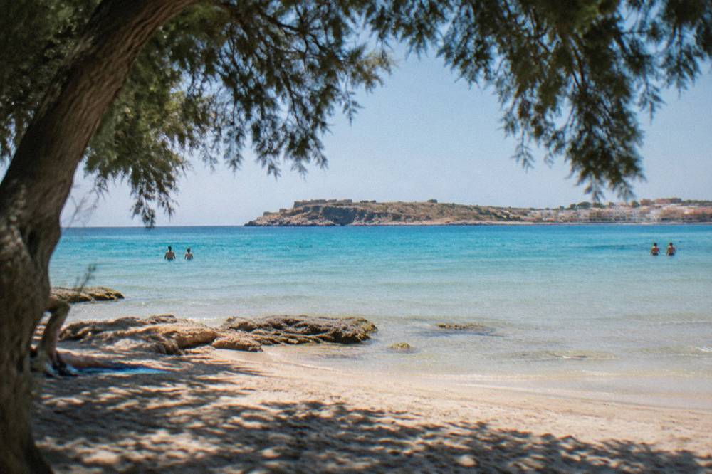 A shallow lagoon with pale sand, turquoise water and a rugged peninsula under a clear sky