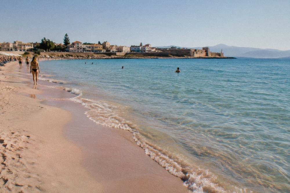 A wide beach with pale pink-tinted sand and shallow turquoise water at the corner of a headland
