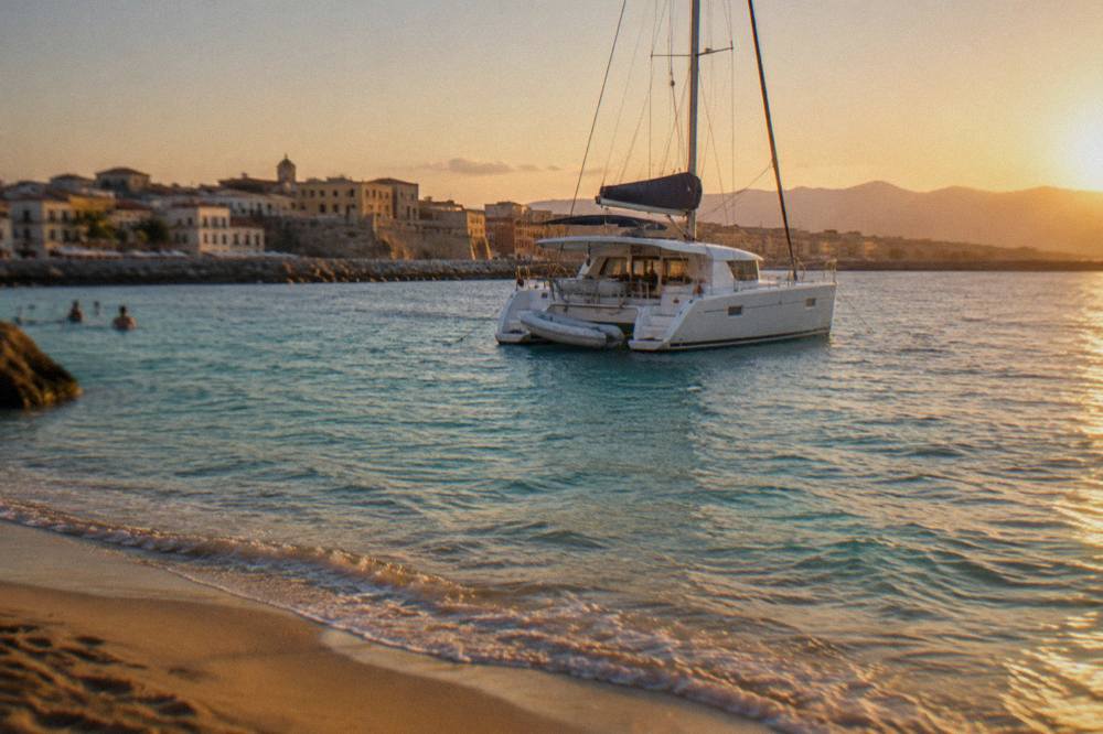 A catamaran anchored in shallow turquoise water near a sandy shoreline
