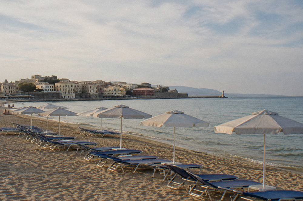 Rows of empty sunbeds and umbrellas on a sandy beach beside calm water