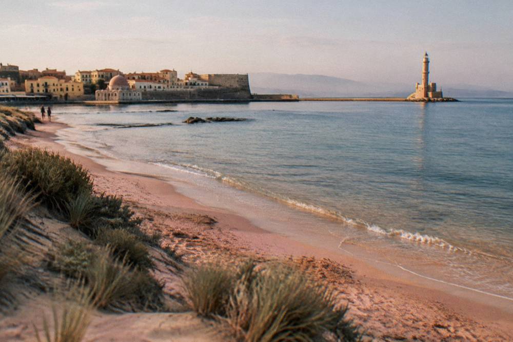 A pink-tinged sandy beach with shallow water and dunes