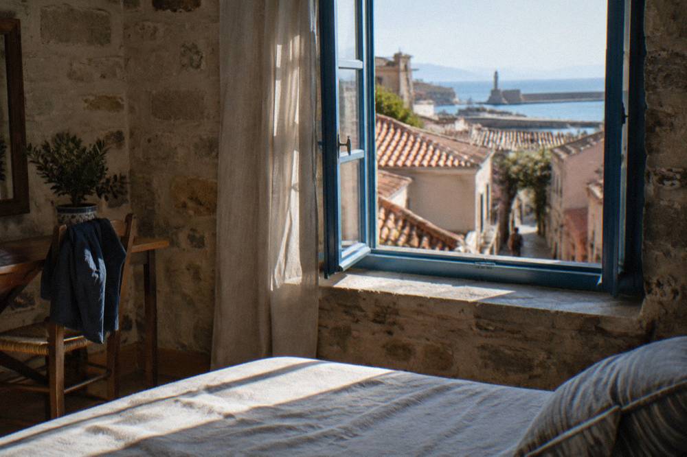 Guest room interior with stone walls and a window overlooking tiled roofs