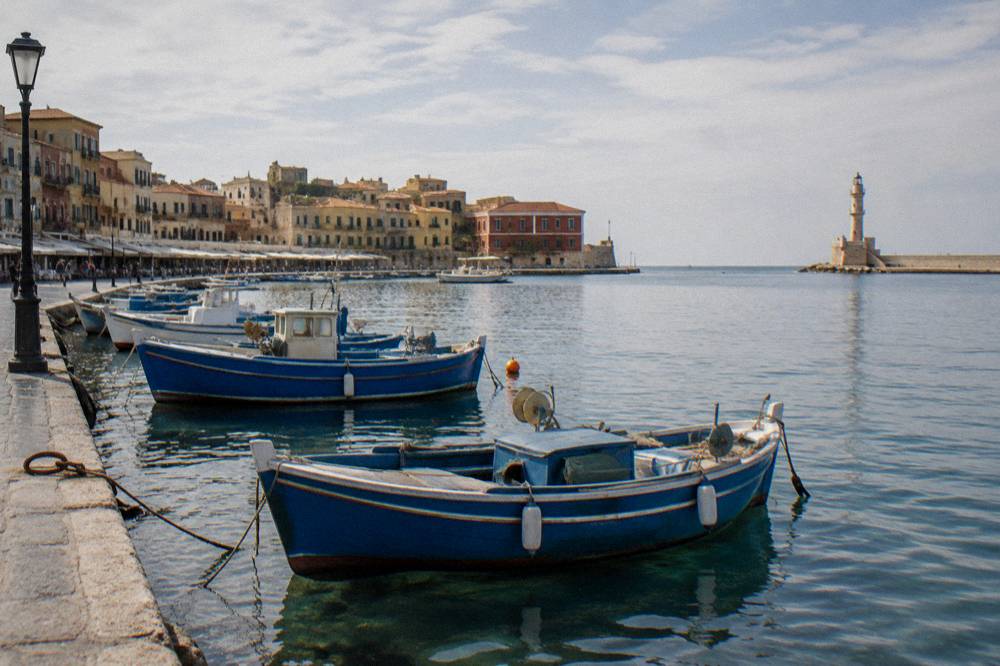 Blue wooden boats moored along the quayside of Chania harbour at midday