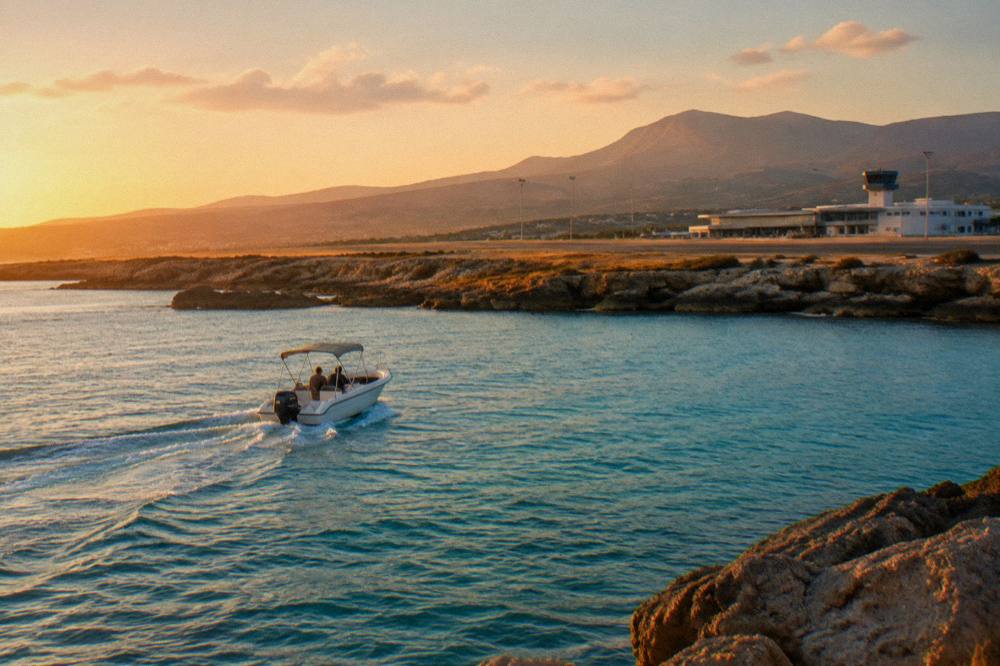A small motorboat crossing clear turquoise water near a rocky coastline