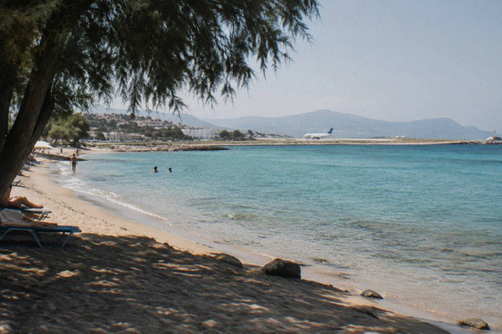 A calm sandy beach with shallow turquoise water near a small Cretan town at midday