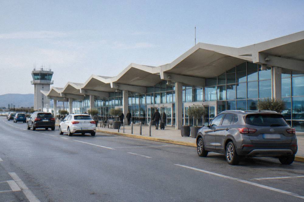 Terminal building of Chania Airport under a clear morning sky with cars at the kerbside