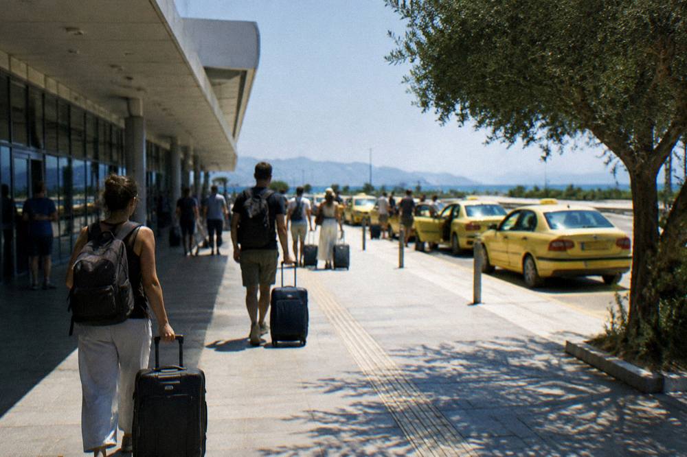 Travellers with luggage walking out of the airport terminal toward a row of waiting taxis
