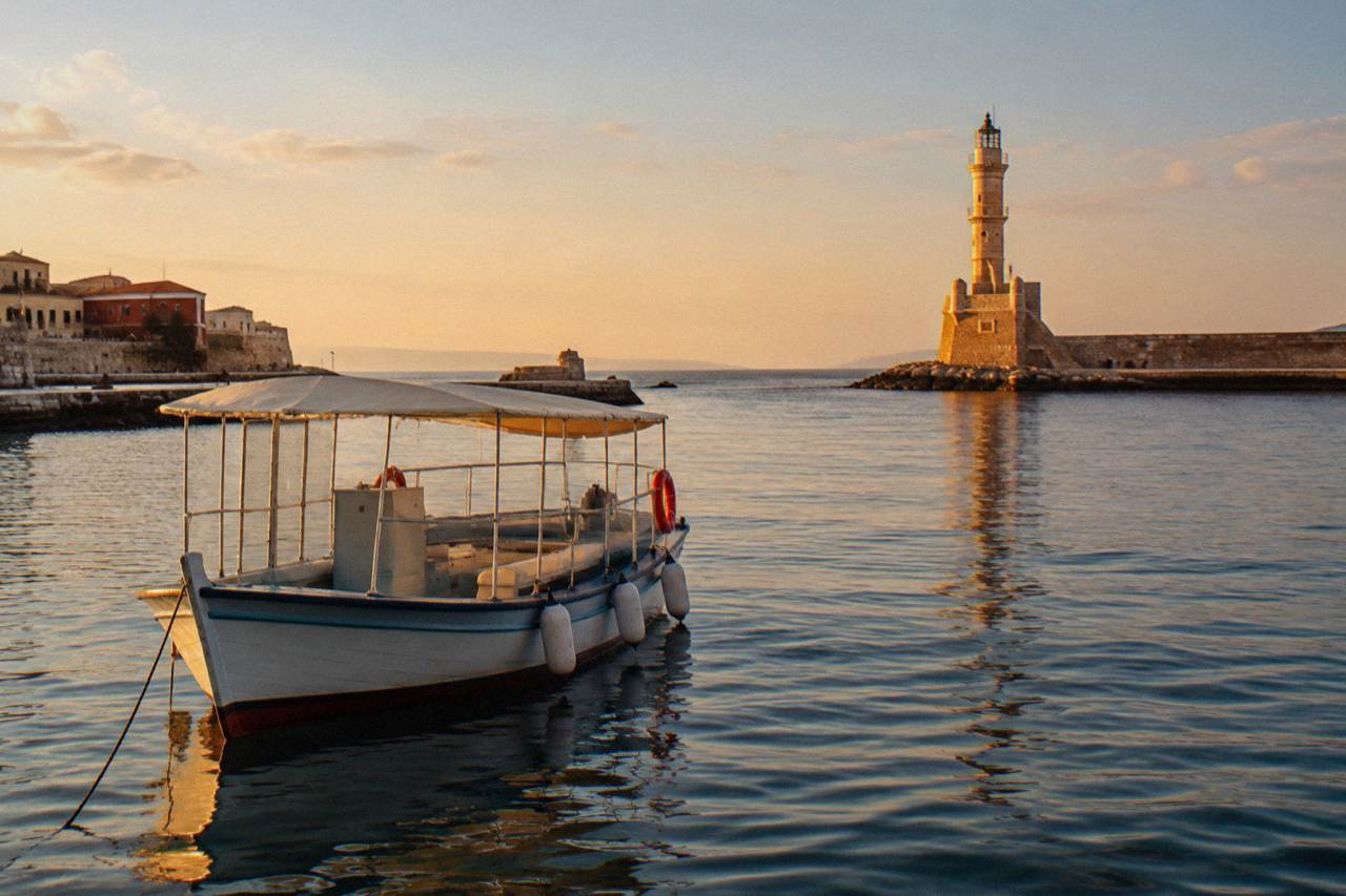 A small excursion boat moored in Chania's Venetian Harbour with the lighthouse in the background