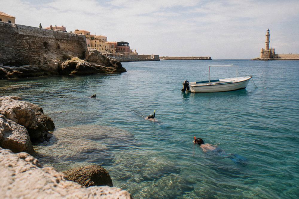 Snorkellers in the water beside a small boat in a rocky Chania bay