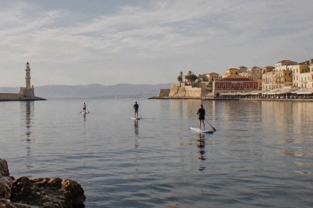 Paddleboarders moving slowly across flat morning water near the Chania coast
