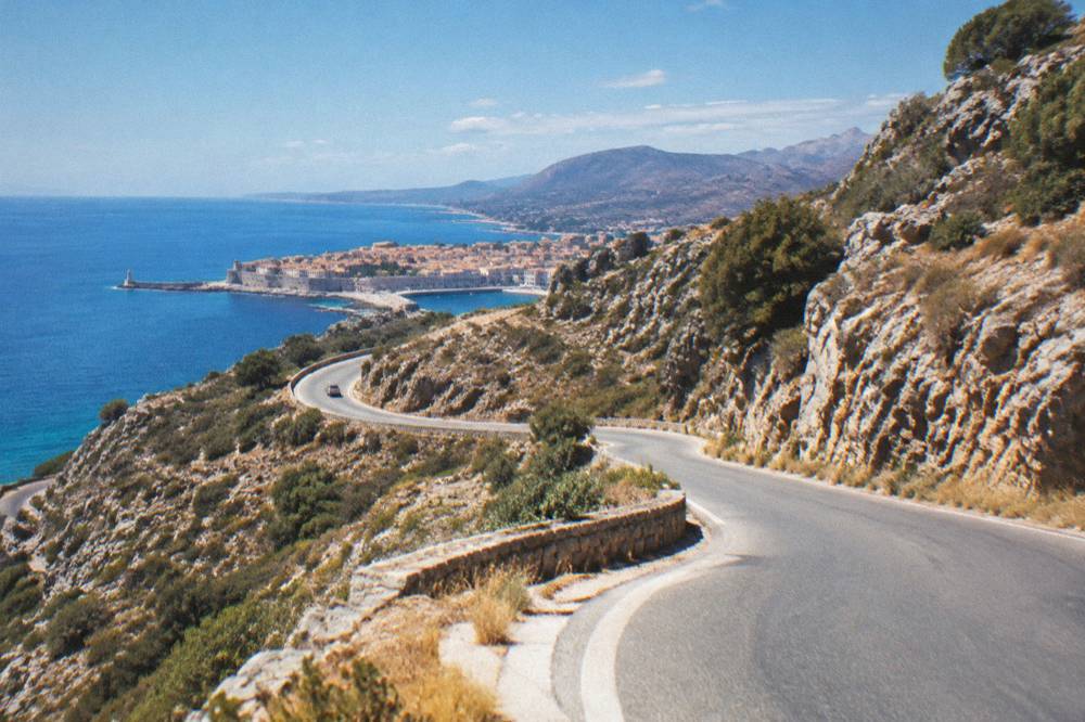 A winding mountain road with hairpin bends climbing through rocky slopes in western Crete