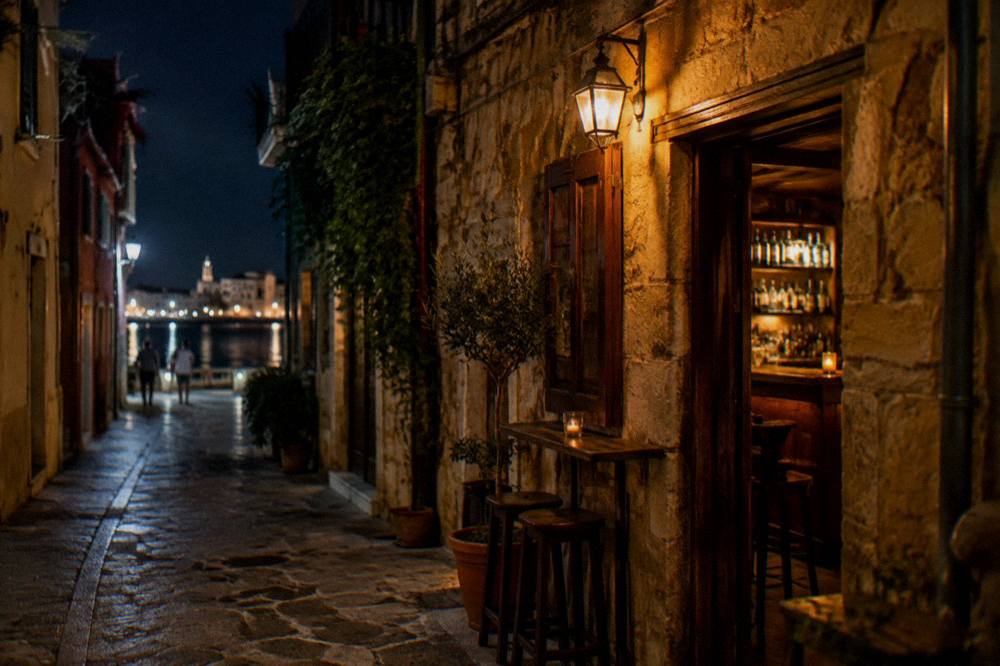 A narrow Old Town lane in Chania at night with warm lamplight over a small bar doorway
