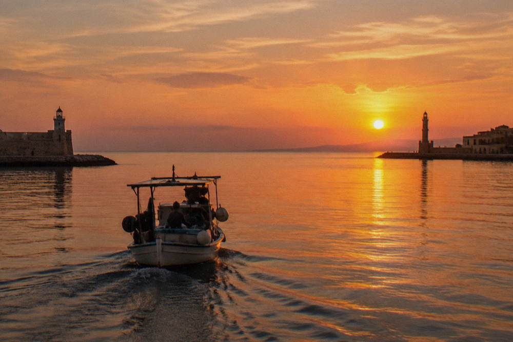 A small boat returning to Chania harbour at sunset with the sea and sky in warm colours