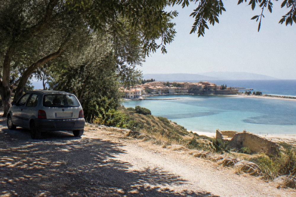 A small parked car on an unpaved gravel road above a coastal lagoon in western Crete