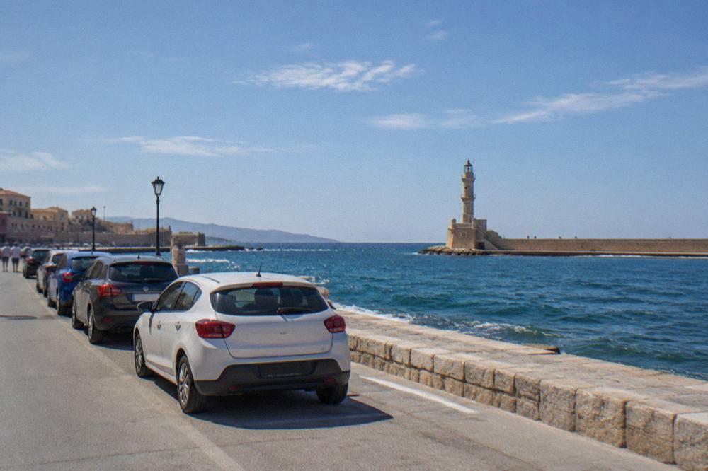 Cars parked along a seafront road with the Chania lighthouse in the distance
