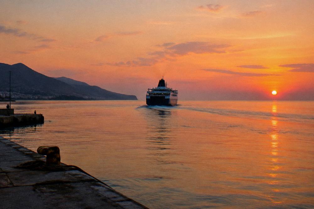 A ferry sailing away from a coastline toward open sea at dusk