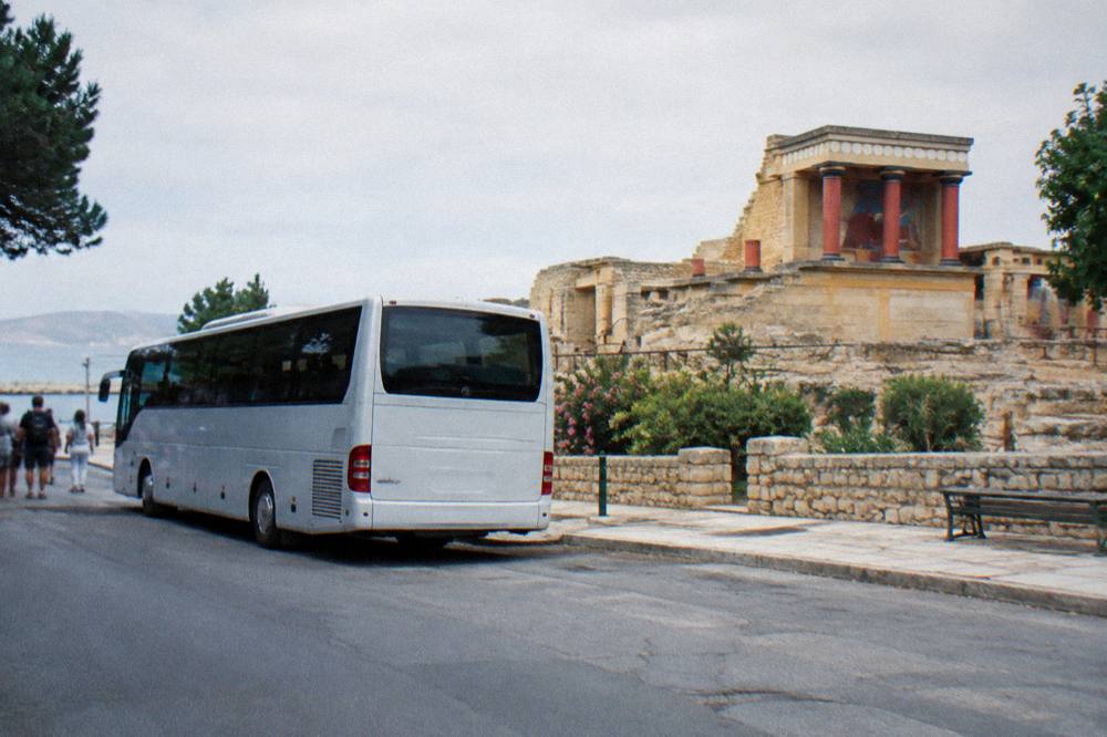 A bus parked at a small street-side station under bright morning light in Chania