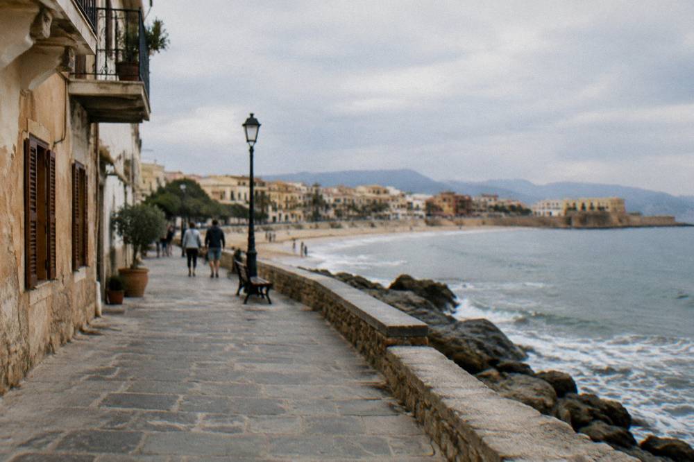 Walking path along the seafront promenade toward a sandy beach near Chania