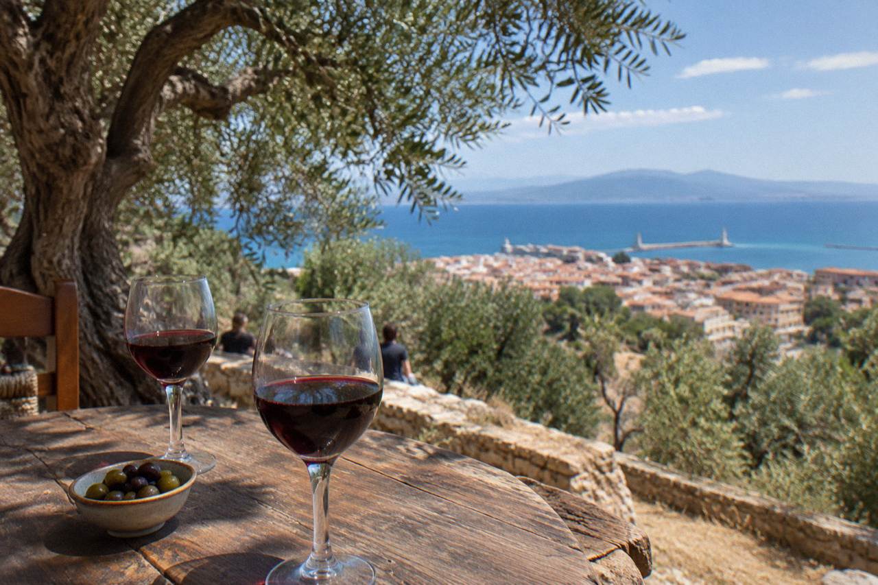 Glasses of red wine on a wooden table beside olive trees on a Cretan hillside