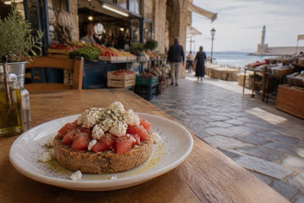 A plate of dakos with barley rusk, chopped tomato, mizithra cheese and olive oil on a wooden table