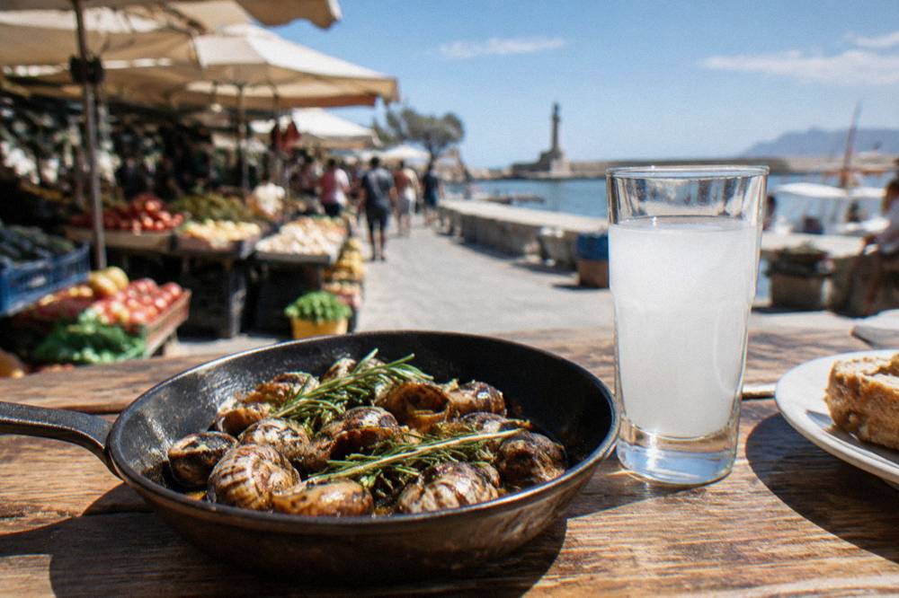 Fried Cretan snails with rosemary in a small pan beside a glass of raki