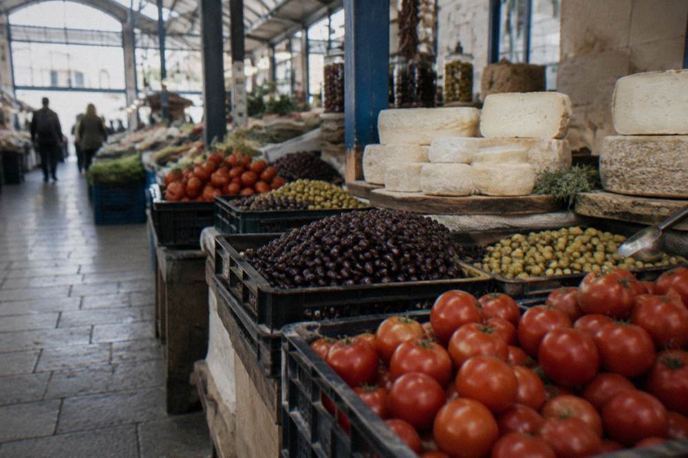 An indoor market stall with crates of tomatoes, olives and rounds of Cretan cheese