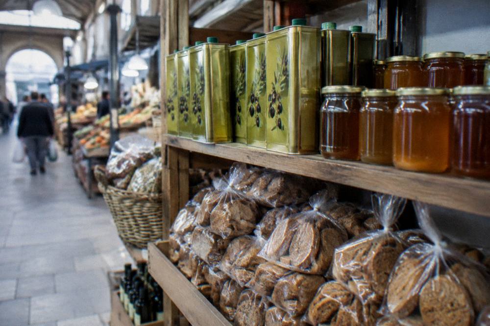 A shop shelf with tins of olive oil, jars of thyme honey and packets of barley rusks