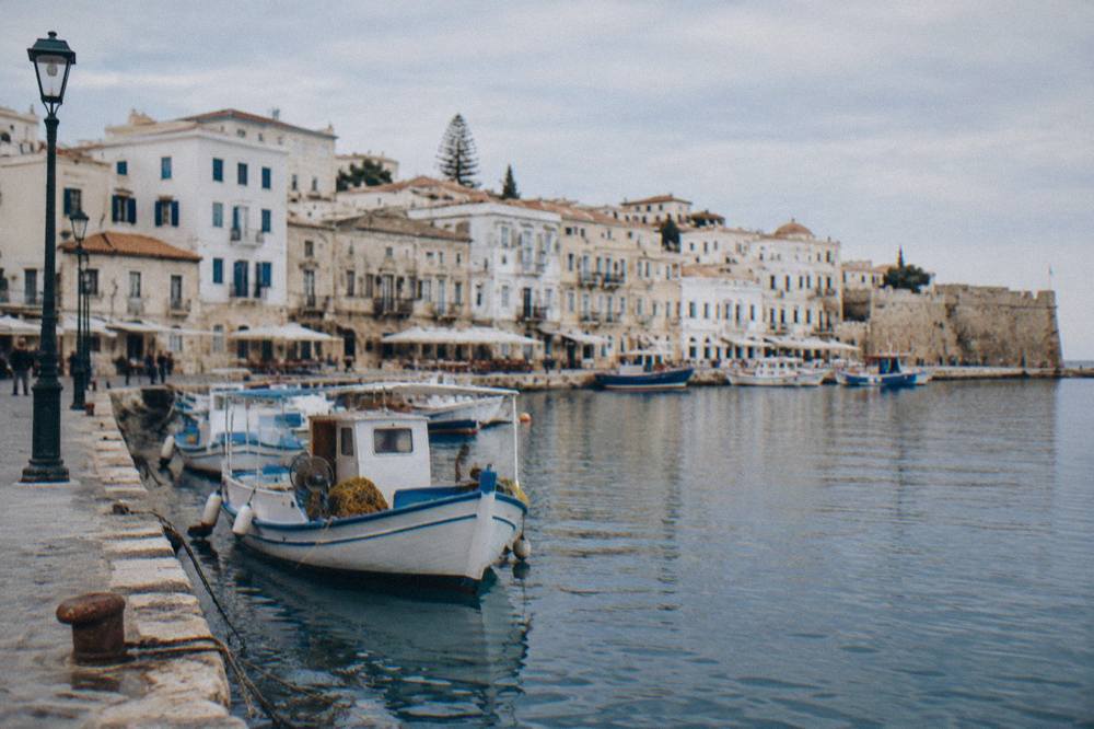 White buildings of Chania Old Town rising behind the harbour quay with fishing boats moored below