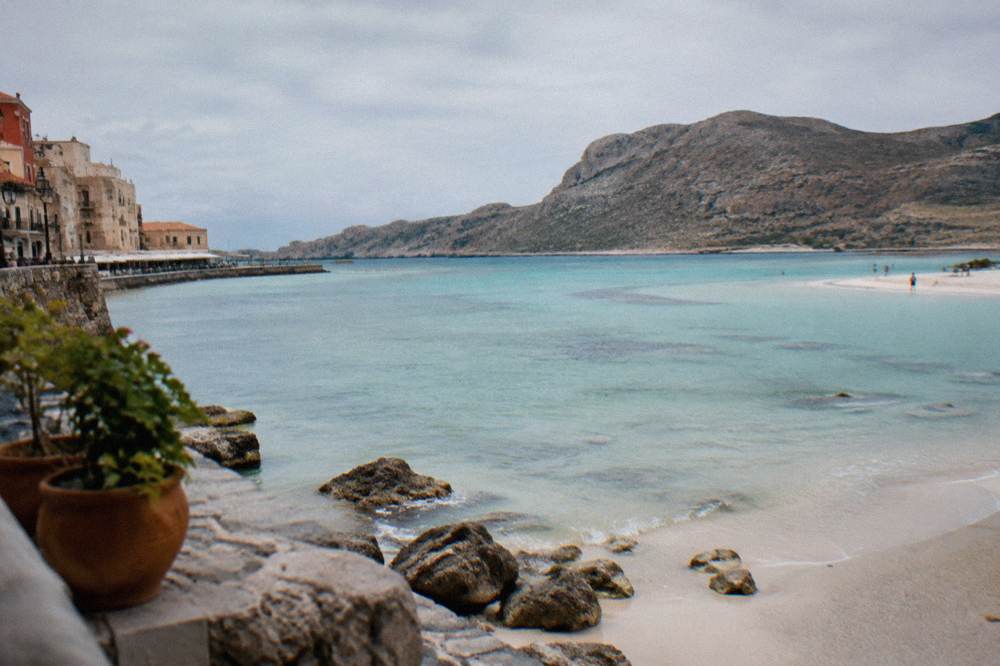 Turquoise shallow water and pale sand of a lagoon beach backed by rocky hills on the Crete coast