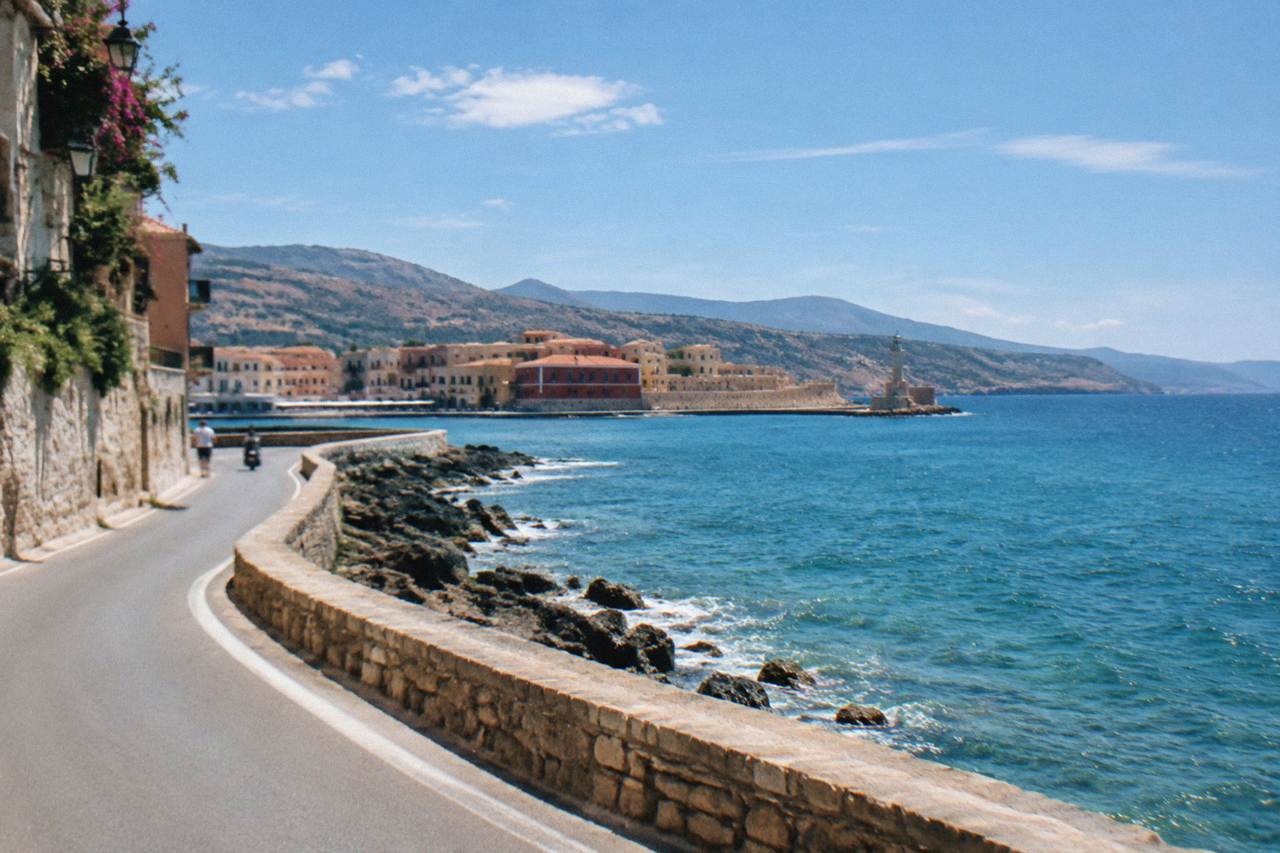 A coastal road curving along the shoreline near Chania with dry hills above the sea
