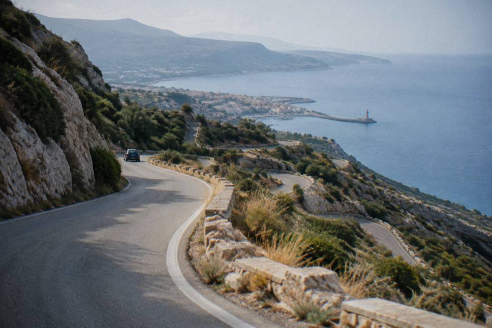 A winding mountain road with hairpin bends climbing through rocky hills in western Crete