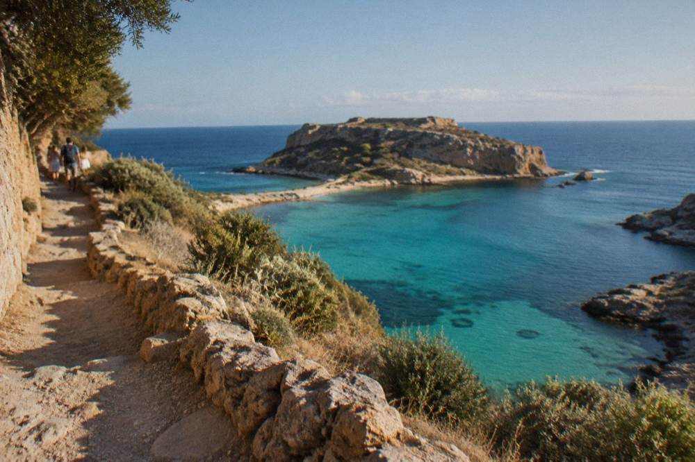A turquoise lagoon and a rocky island seen from a cliff path above the sea