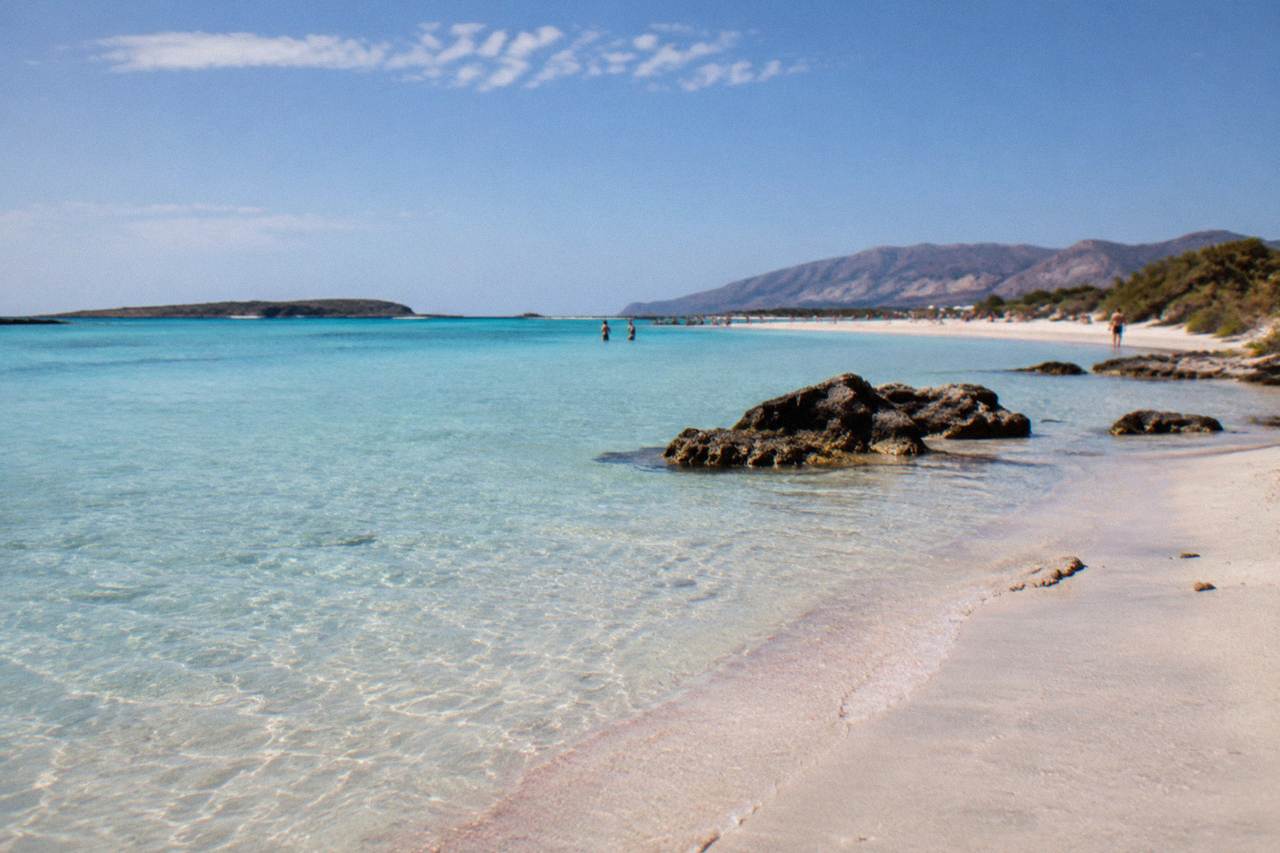 A wide lagoon of shallow turquoise water beside a pale sandy beach under a clear sky