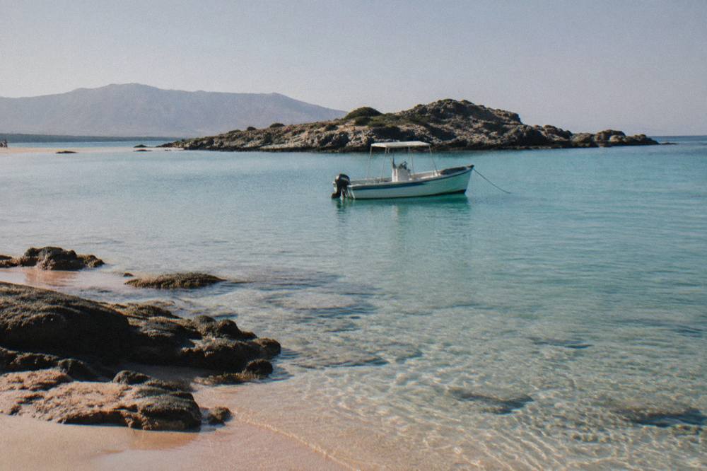 A boat anchored in clear shallow water near a rocky island