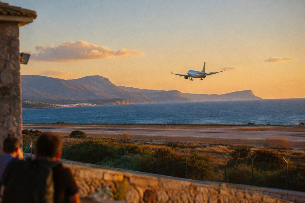 A passenger aircraft descending over blue sea toward the coast of Crete