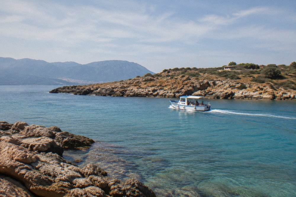 A small boat cruising along a coastline of clear shallow water and rocky headlands