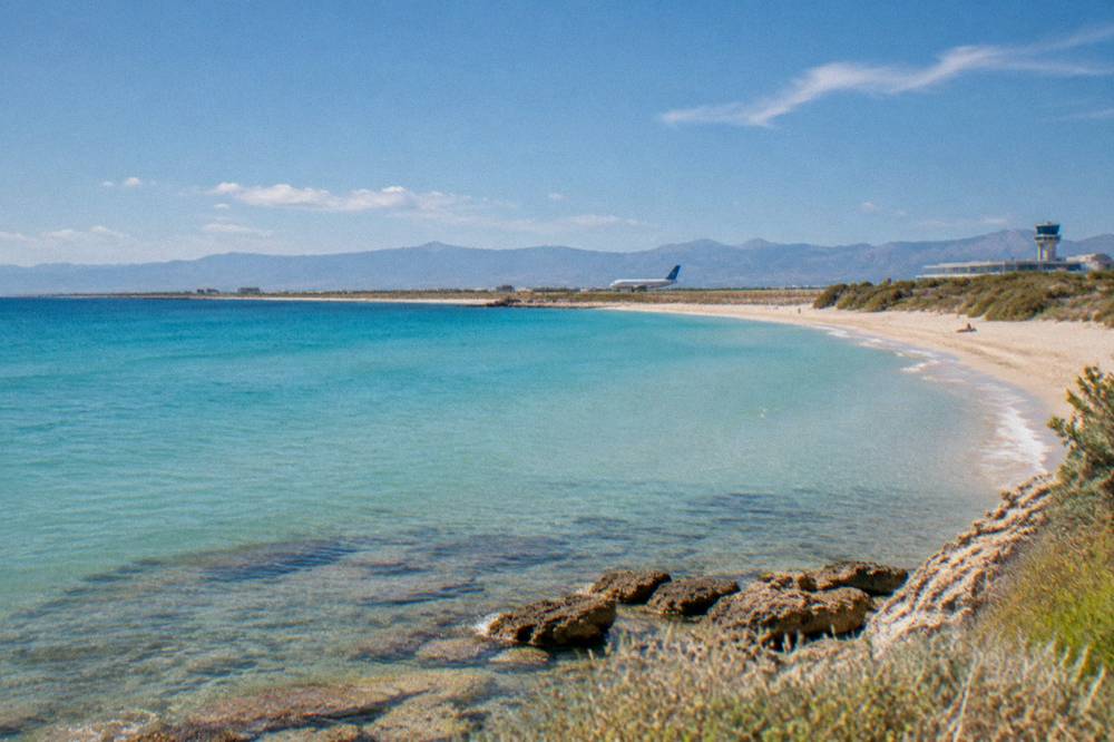 A quiet beach with turquoise shallows under a warm morning sky in late spring