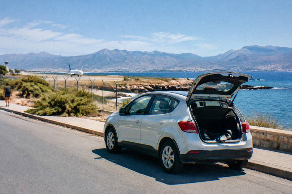 A rental car parked beside a coastal road with the sea and hills in the distance